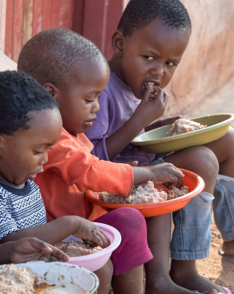 Yer sofrasında elleriyle kaseden basit yemek yiyen çocuklar